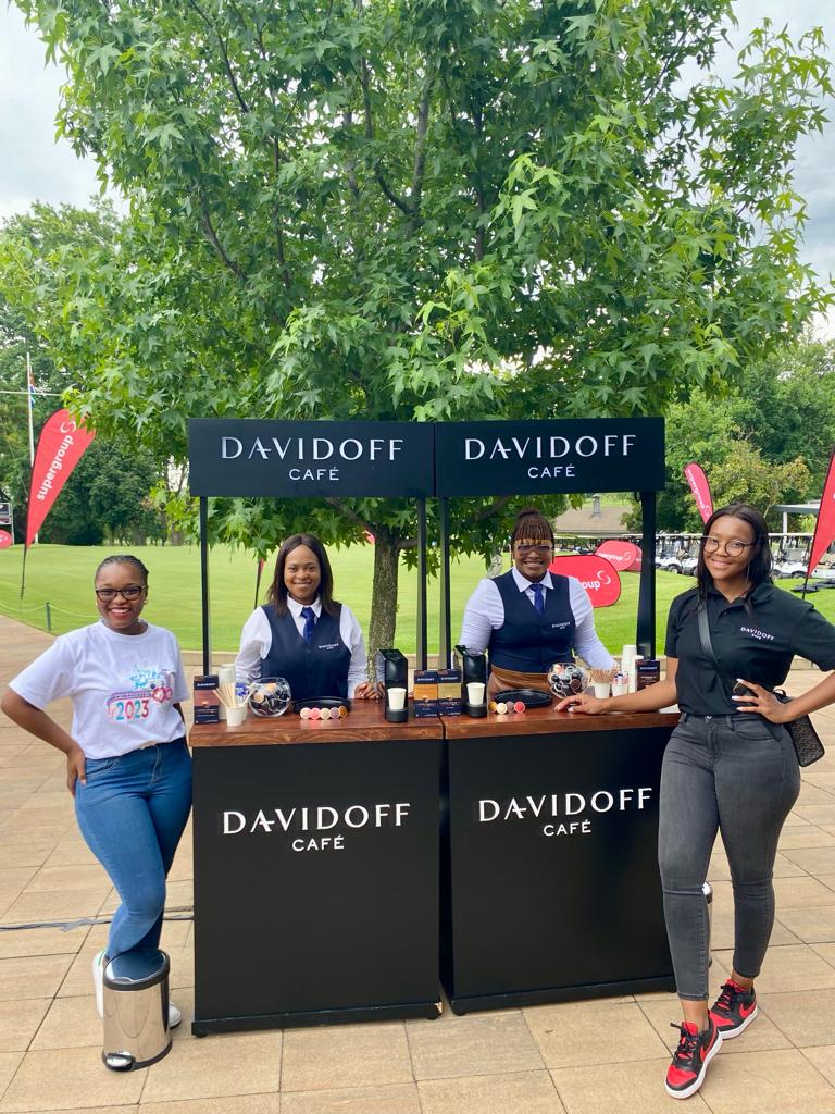Isilumko-Activate Four people standing at a davidoff cafe instore brand ambassadors booth outdoors, with two wearing promotional t-shirts and two in black outfits.