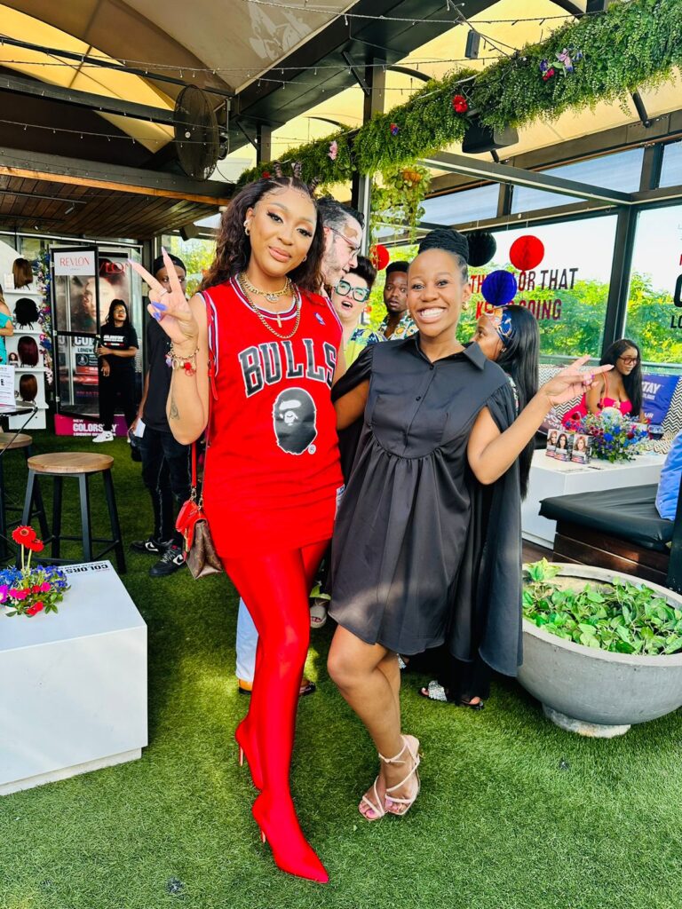 Isilumko-Activate Two instore brand ambassadors smiling for the camera at an outdoor event, one dressed in a Chicago Bulls outfit and red boots, the other in a black dress.